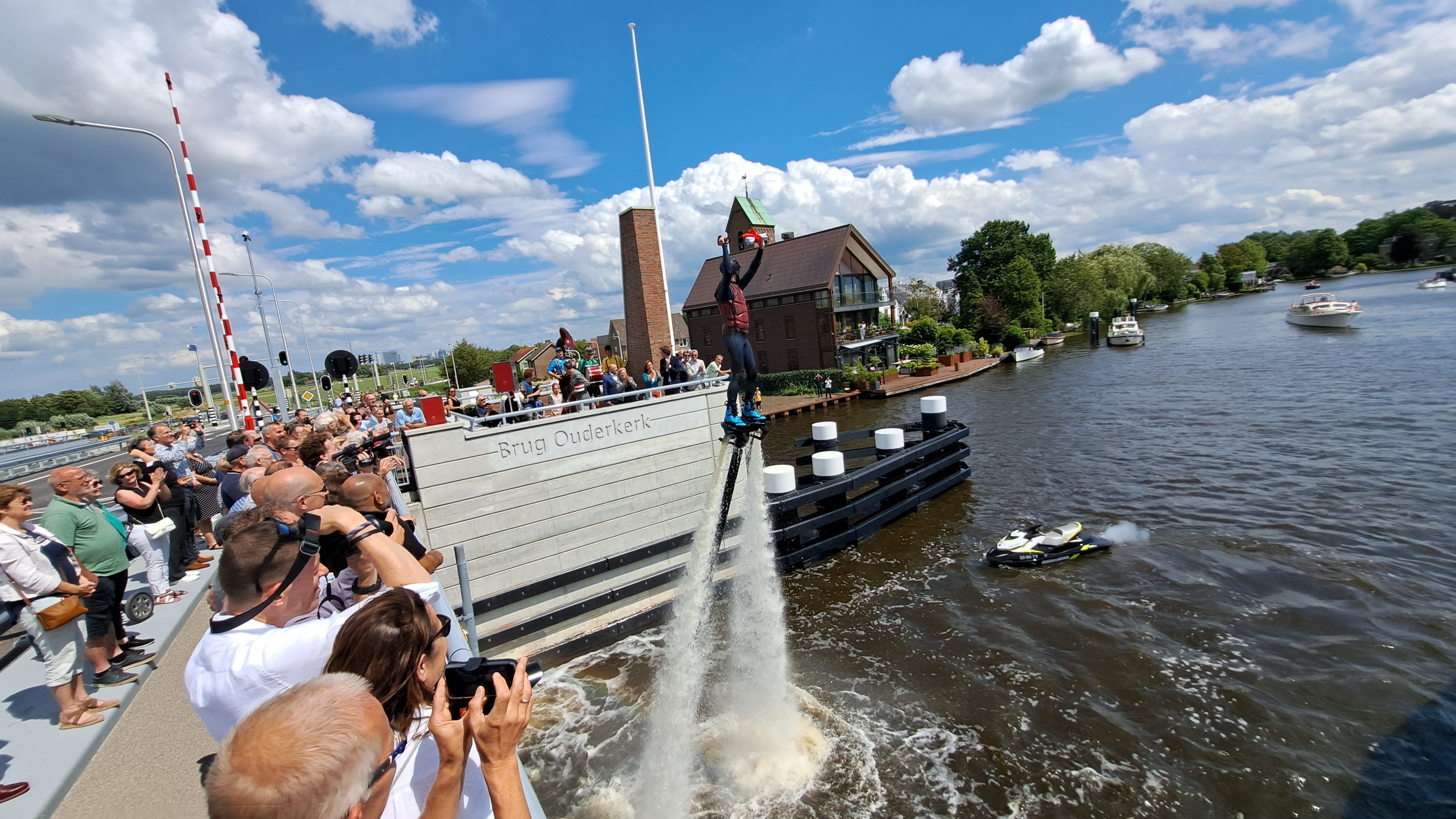 Foto 4: De flyboarder heeft de vlag voor de opening in zijn hand. Velen bekijken de capriolen van de flyboarder.