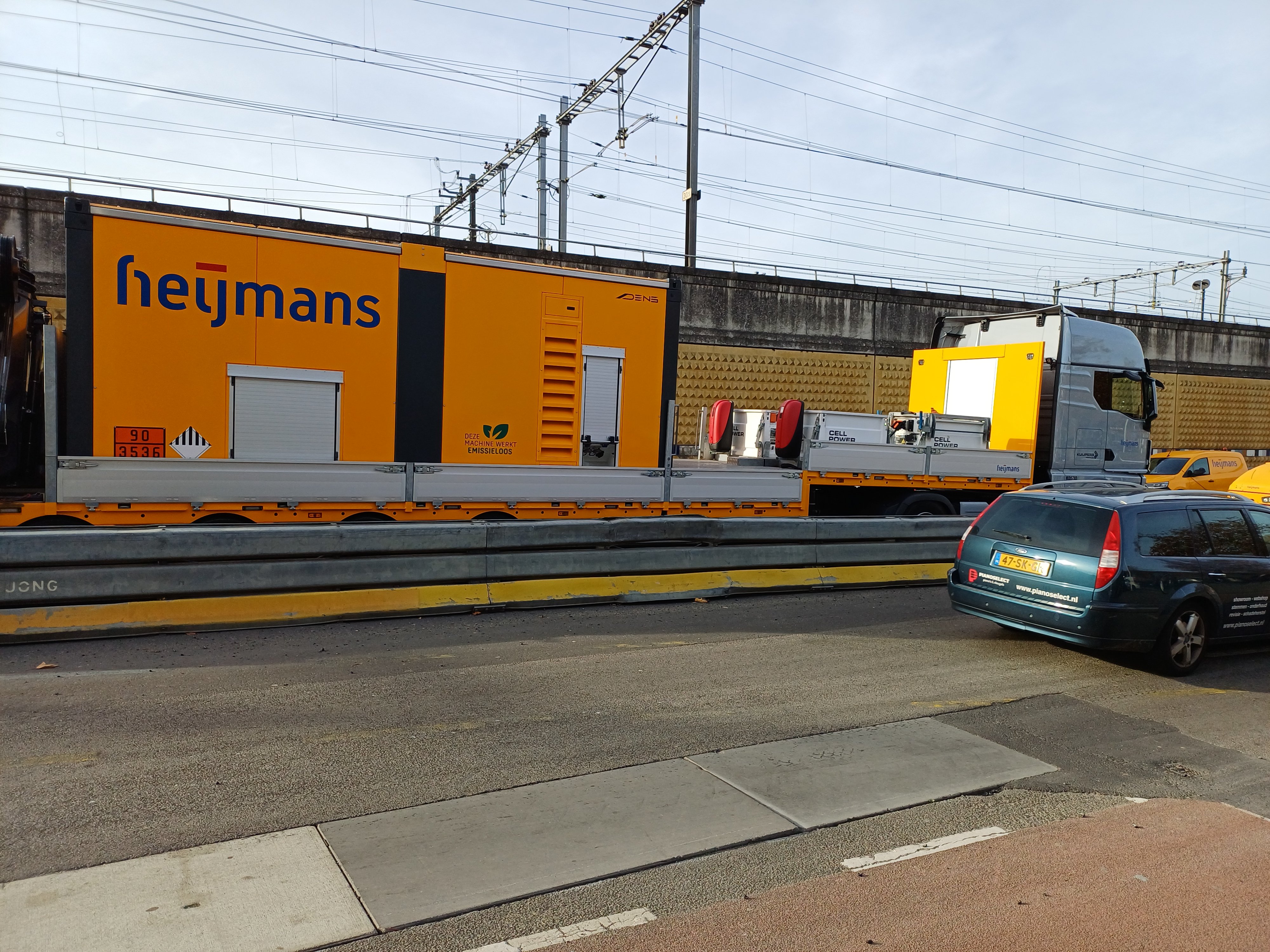 Vrachtwagen met wisselbatterijen voor asfaltmachine en wals.