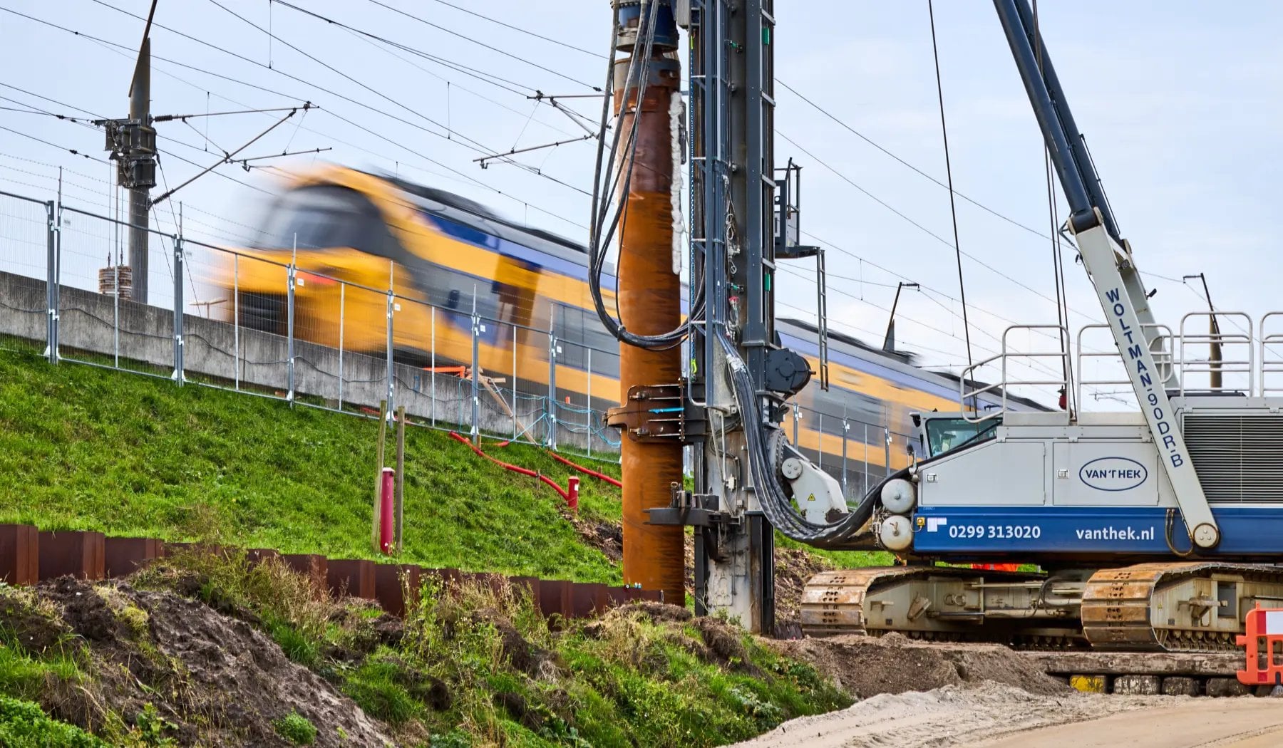 De eerste paal wordt de grond in gedraaid terwijl het spoorverkeer gewoon doorrijdt.