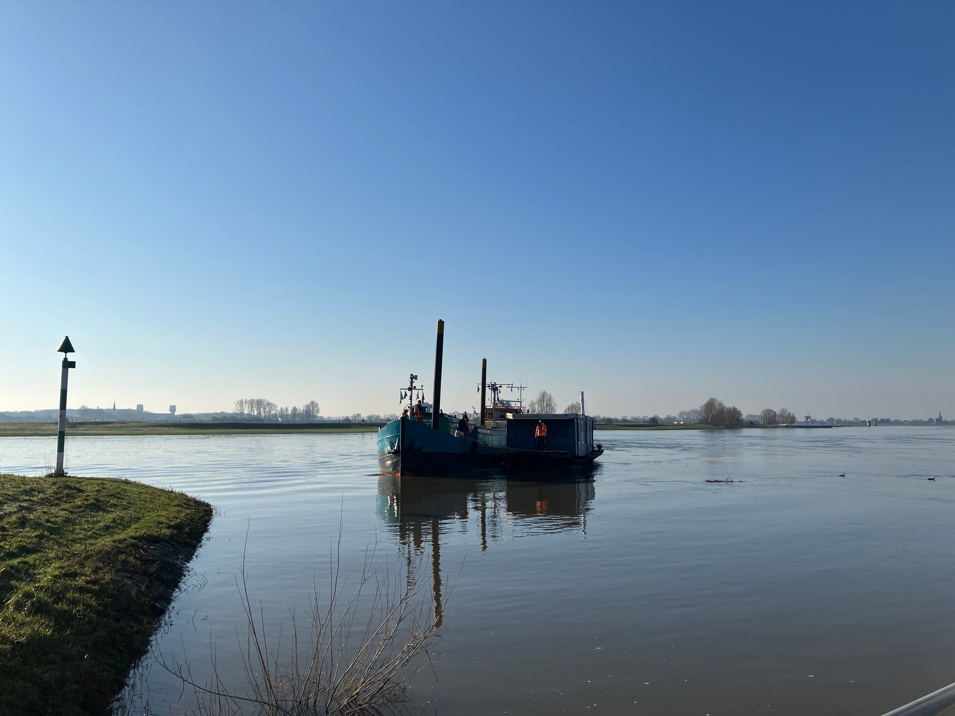 Het kraanschip van Van Beest Maritiem begeleidt de woonboot in de ochtendzon naar de haven van Wijk bij Duurstede.
