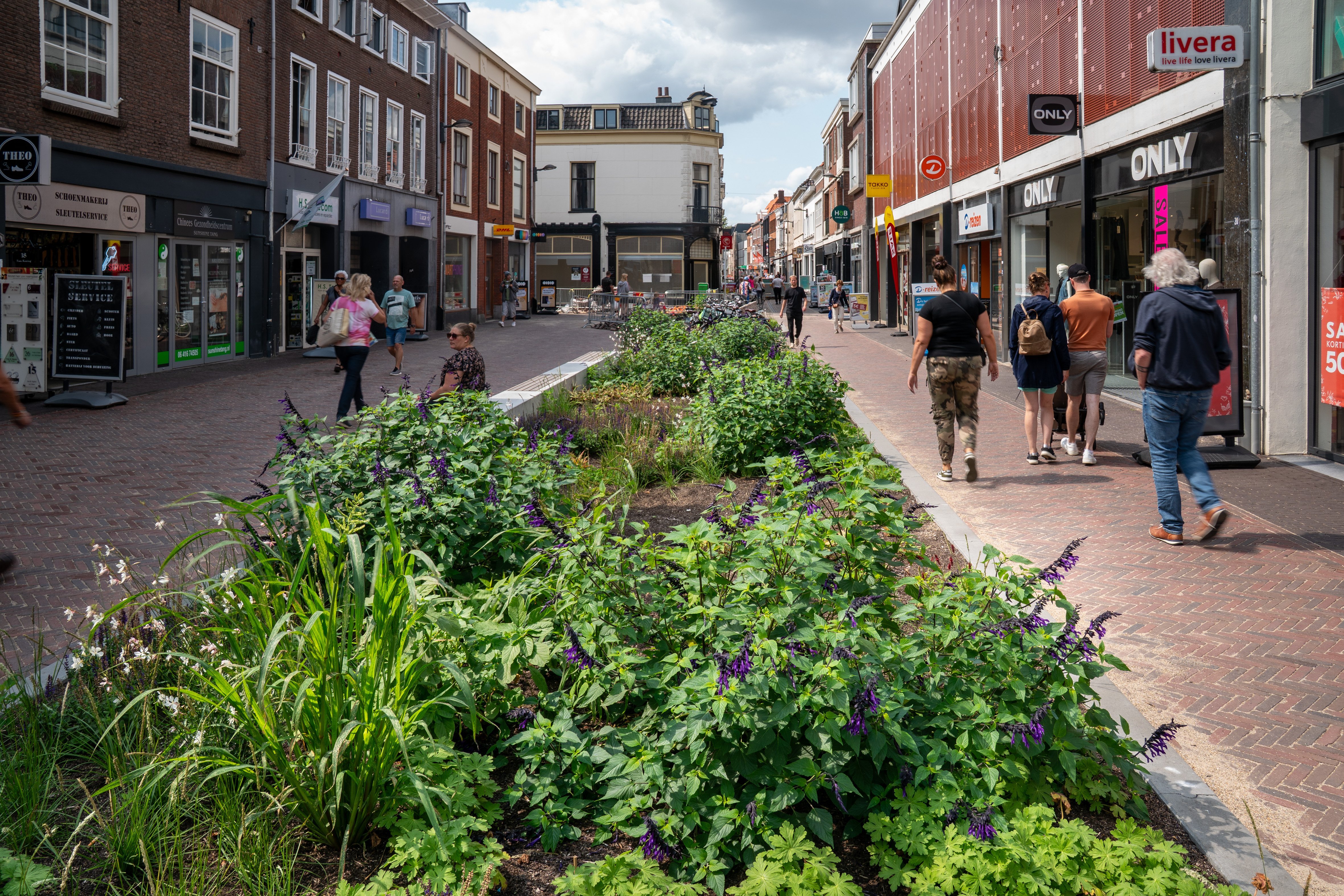 Op de afbeelding is een plantenvak op de Waterstraat zichtbaar en voetgangers die rondom het plantenvak lopen.
