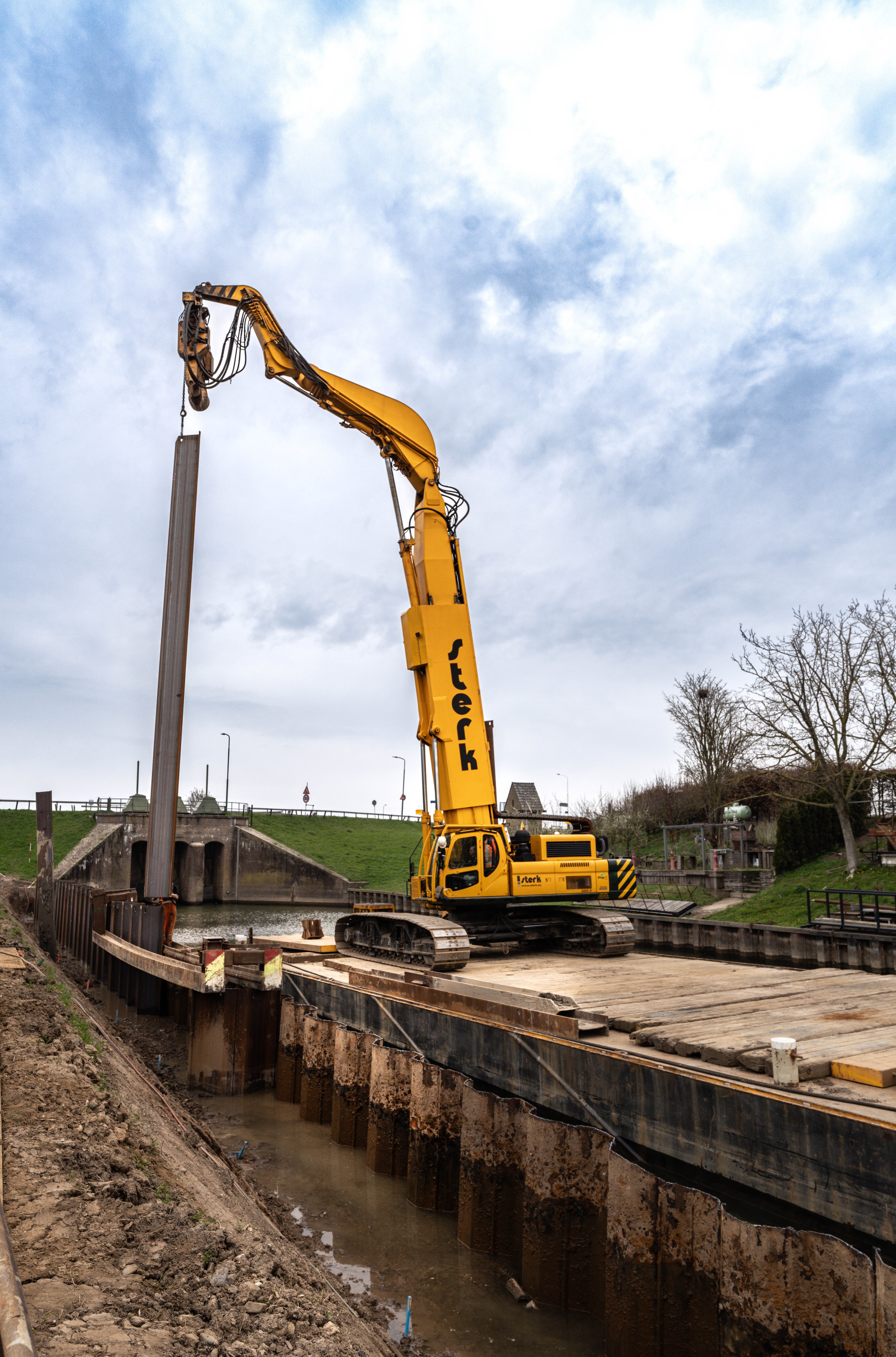 In het Inundatiekanaal plaatst een kraan vanaf een ponton de damwandplanken.