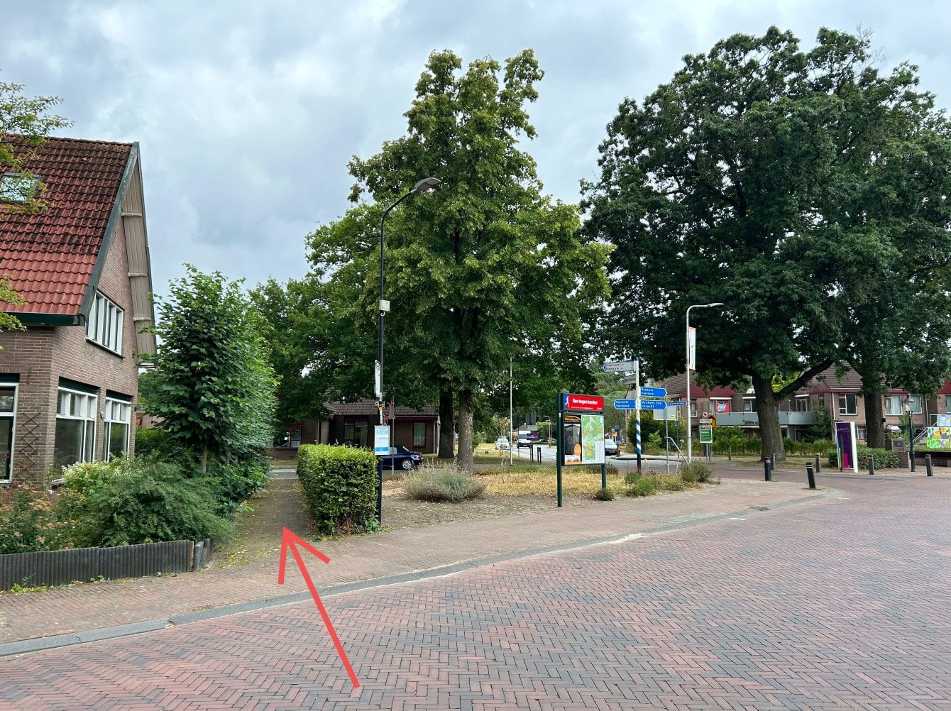 Voetgangers worden gestuurd door het paatje langs de heg zoals aangegeven met de rode pijl zodat het dorpsplein en Pro Persona terrein bereikbaar blijven.
