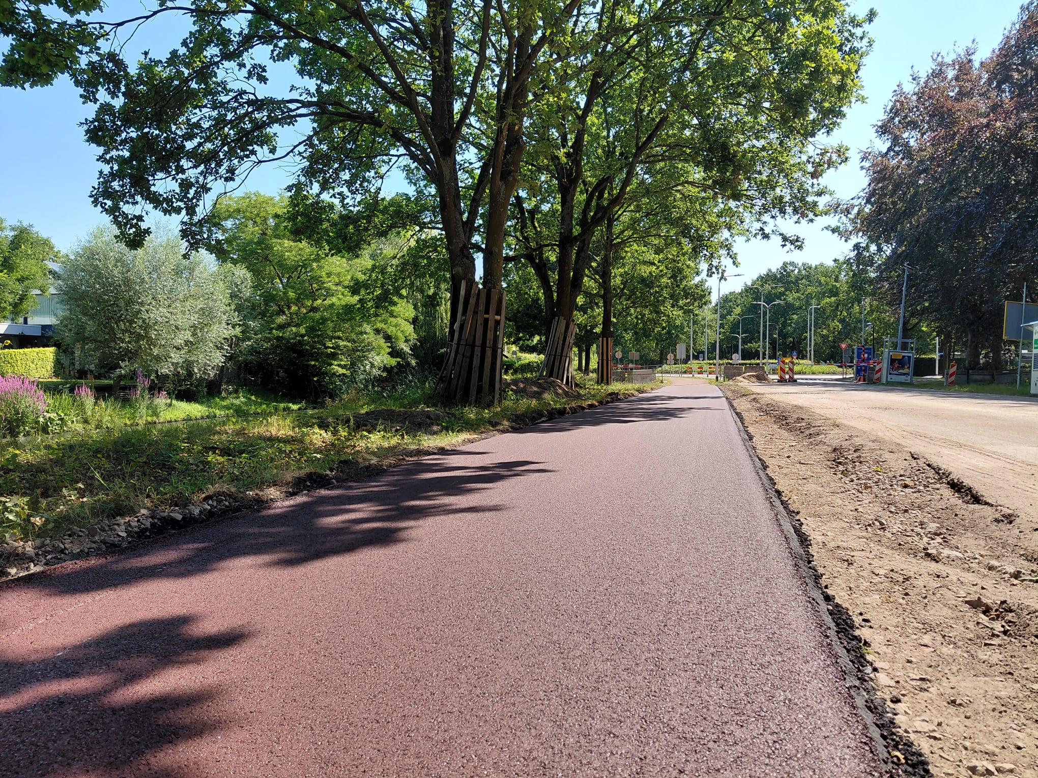 Op de afbeelding is het nieuwe asfalt van het fietspad te zien met op de achtergrond de slagbomen bij rotonde Deltalaan - Gilzerbaan.