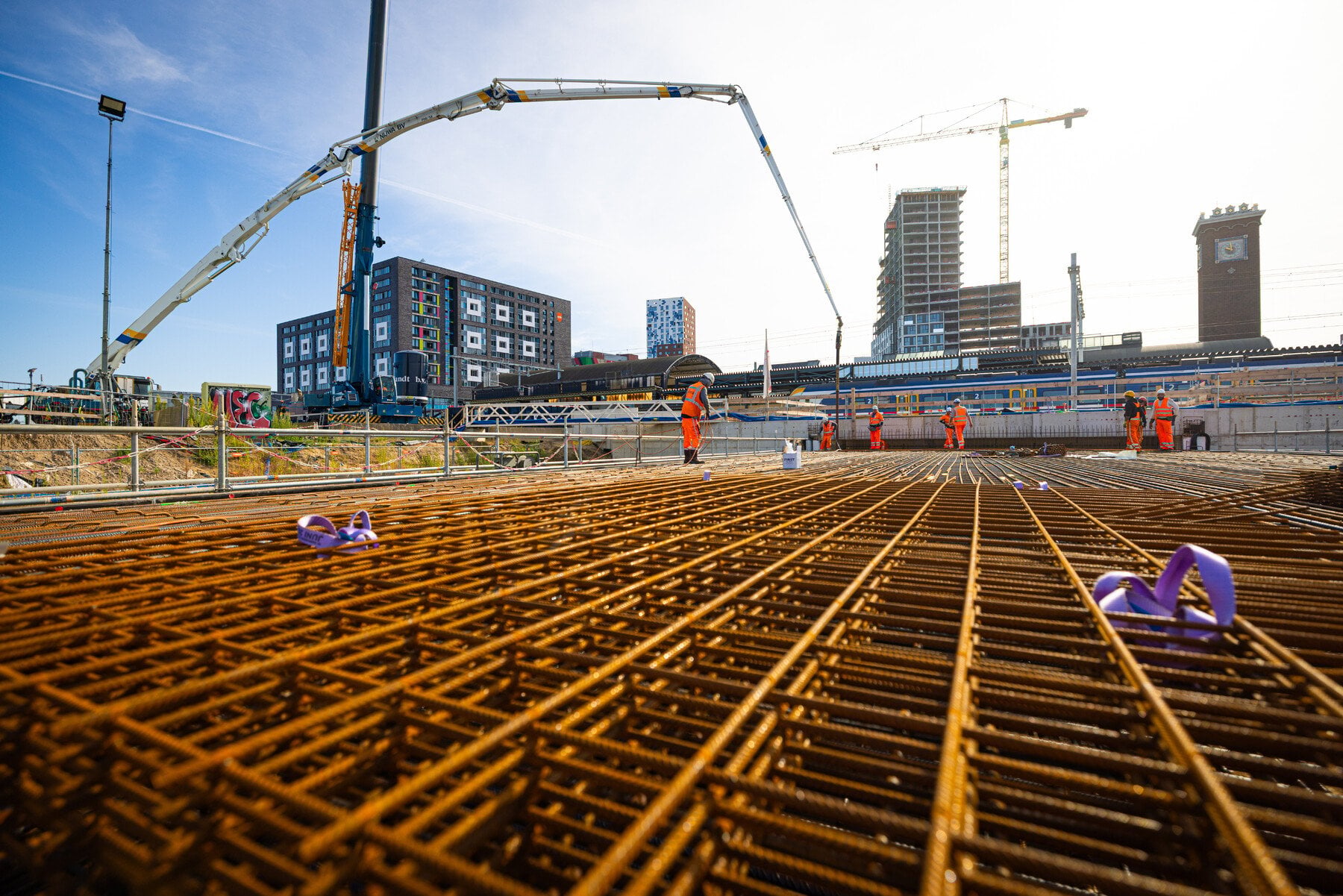 Op de voorgrond zie je de wapening van dichtbij. Op de achtergrond staat de betonpomp klaar om beton te storten.
